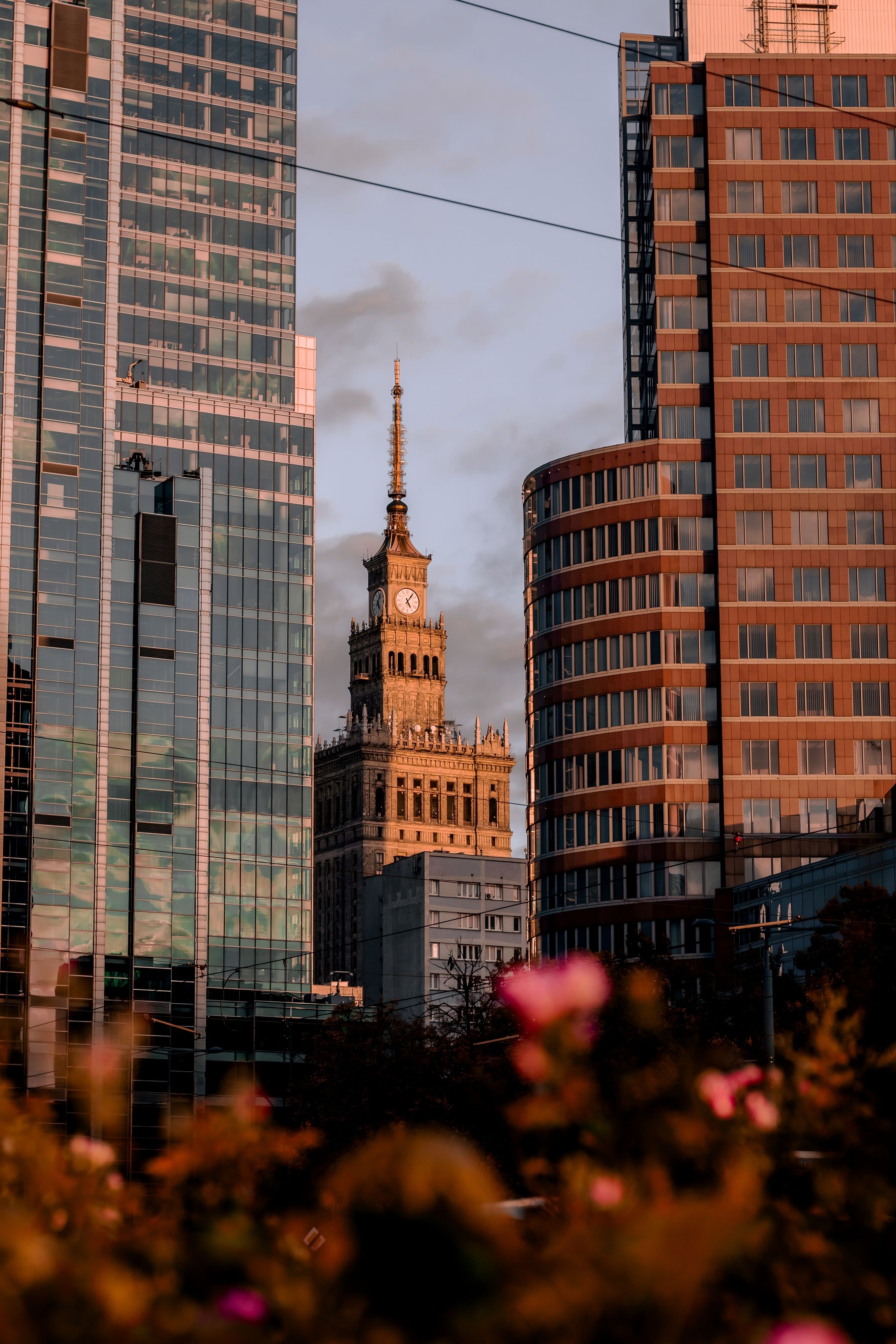 View of Warsaw's Palace of Culture and Science framed by modern skyscrapers at sunset.