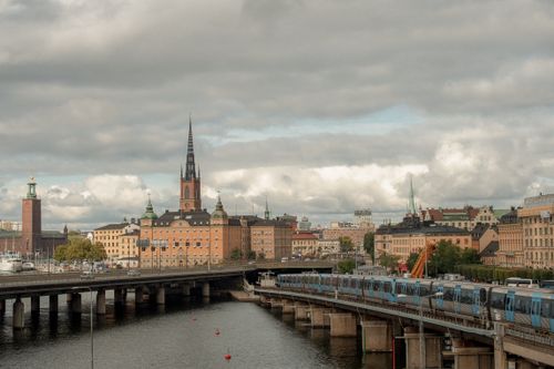 Free Dynamic view of Stockholm featuring a train, historic buildings, and a church spire under cloudy skies. Stock Photo