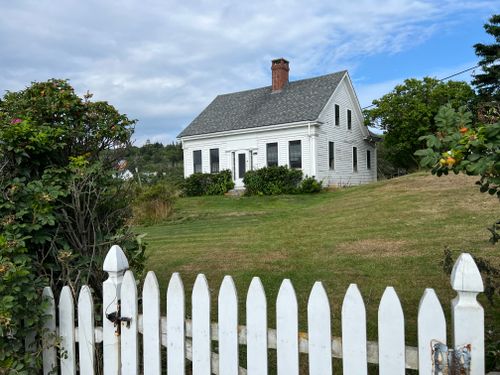 Free Quaint white cottage with picket fence and lush garden, perfect for a serene coastal retreat. Stock Photo