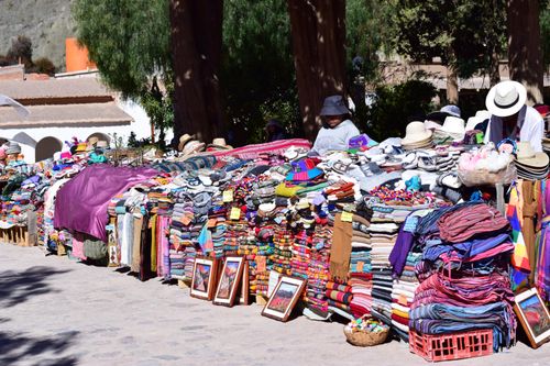Free Vibrant outdoor market stall showcasing colorful textiles, hats, and other handmade goods in a sunny setting. Stock Photo