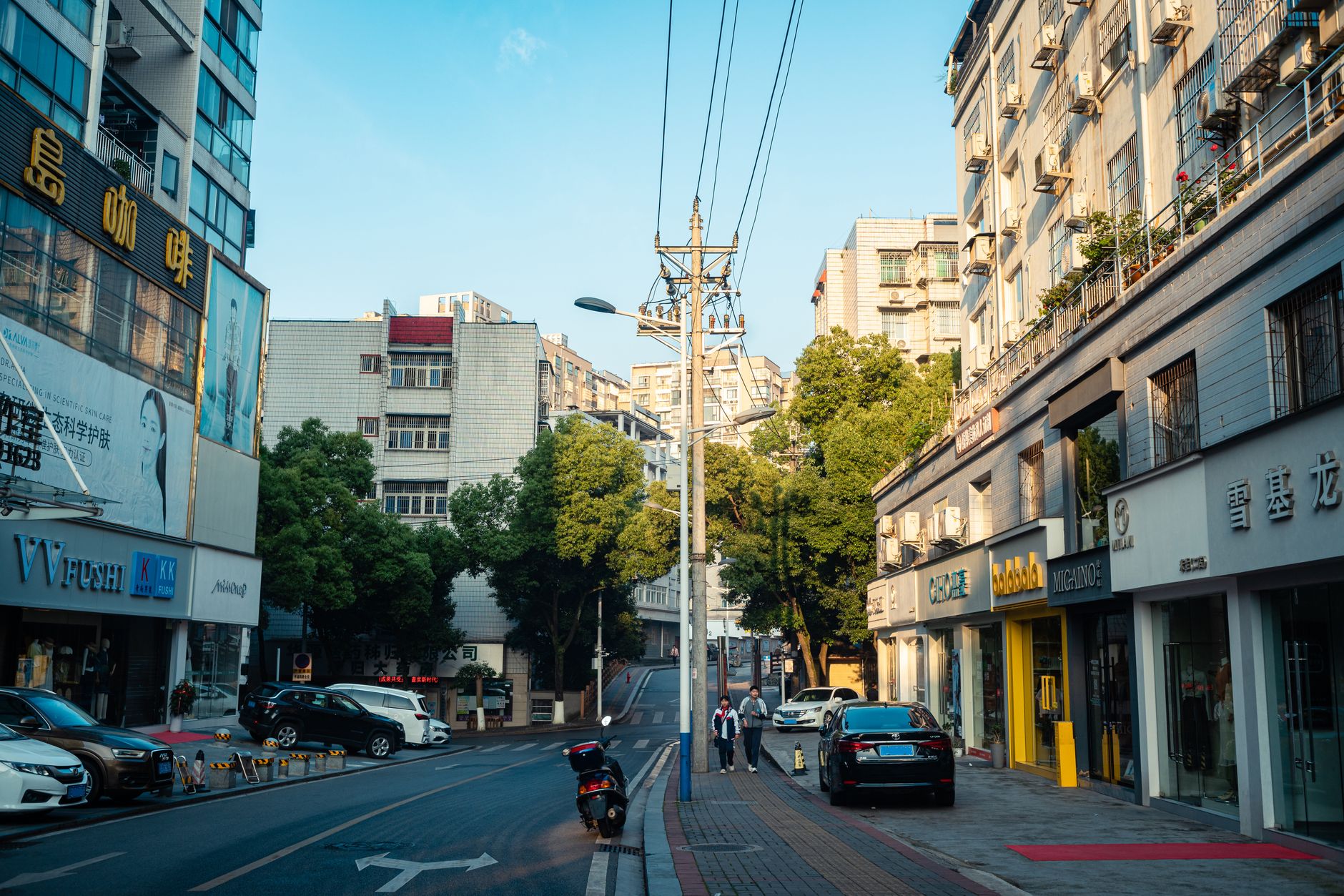 A quiet city street with cars and pedestrians in early morning sunlight.