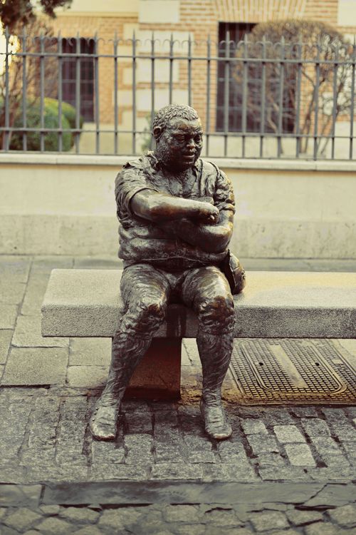 Free Bronze statue of a seated figure on a stone bench in Spain. Stock Photo