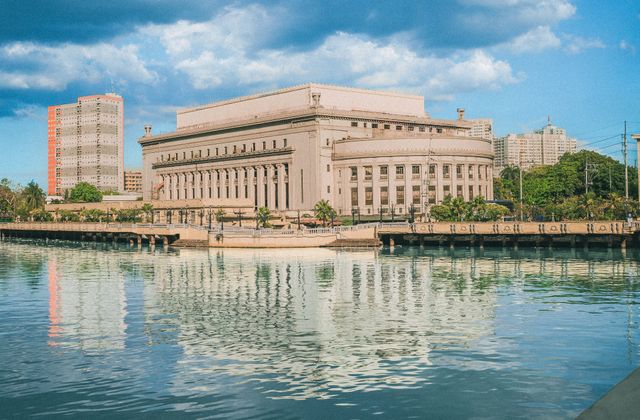 The iconic Manila Post Office building reflecting on the Pasig River under a bright blue sky. — arriving in Manila