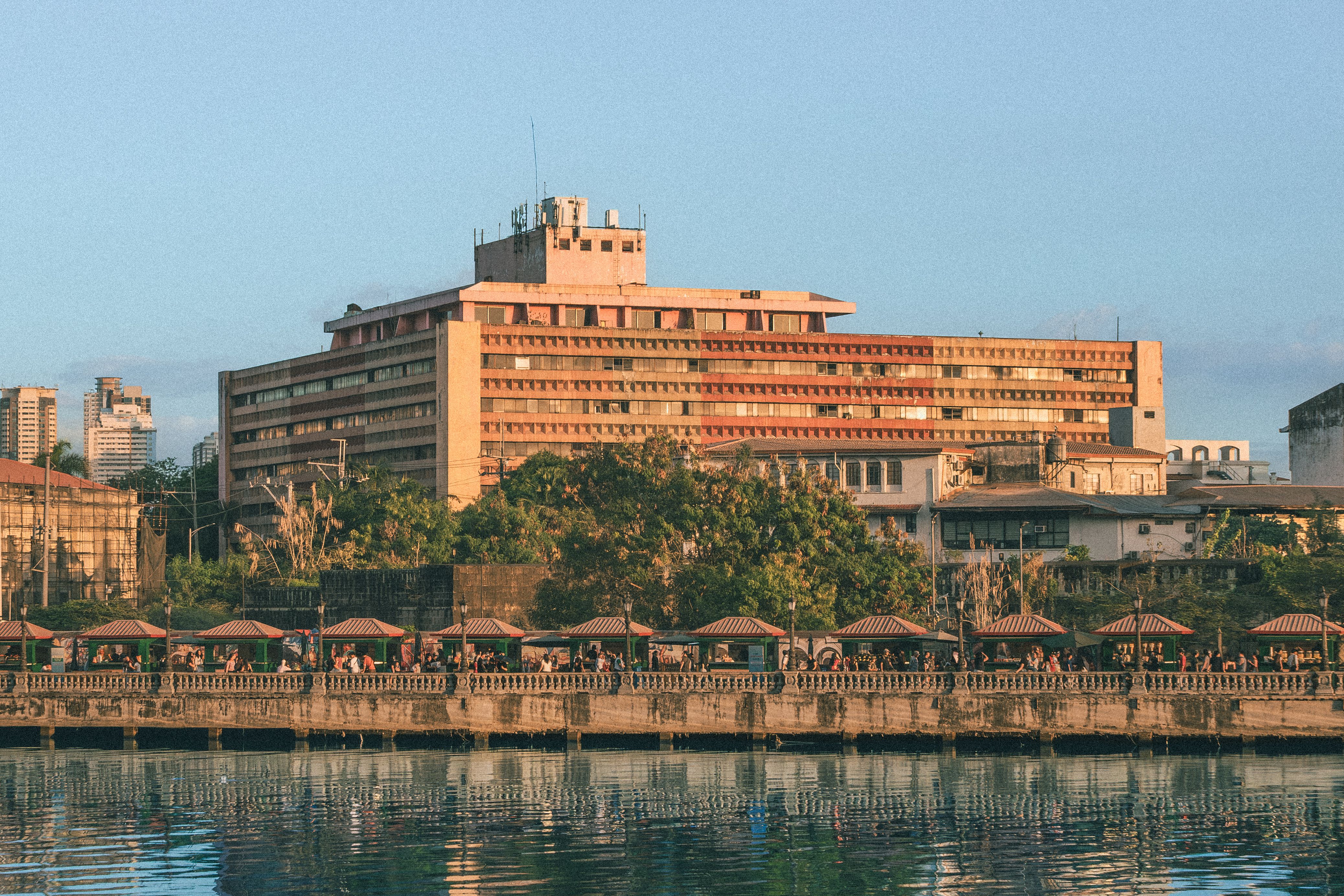 A scenic view of a historic riverside building in Manila during sunset, reflecting urban life.