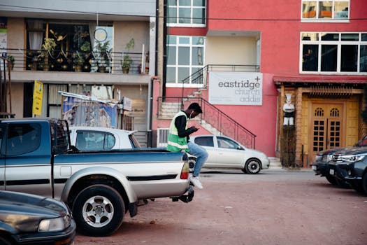 Man wearing a vest sitting on a pickup truck texting on a street near Eastridge Church Addis building.