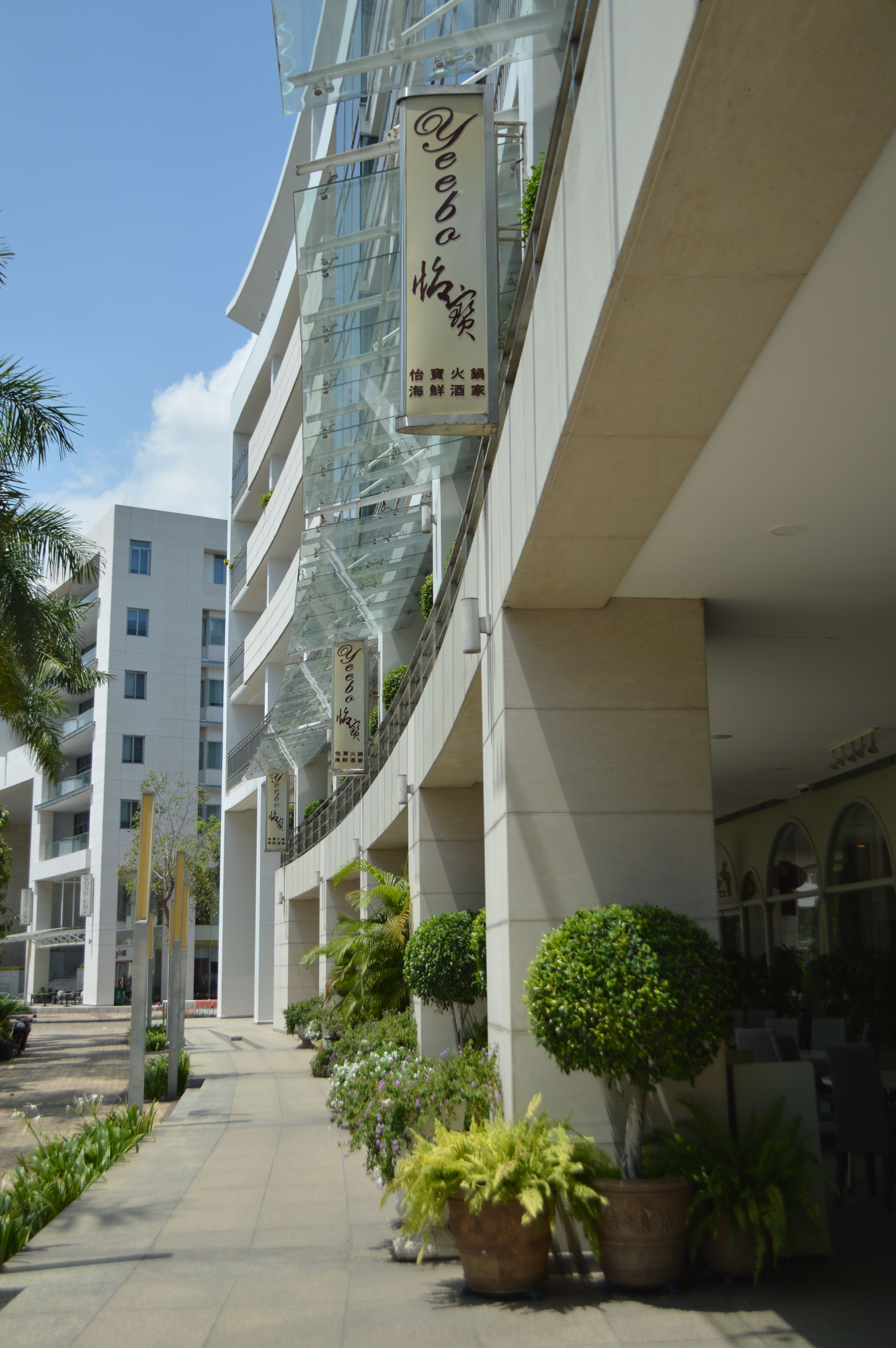 Elegant contemporary building exterior featuring prominent signage and lush greenery on a sunny day.