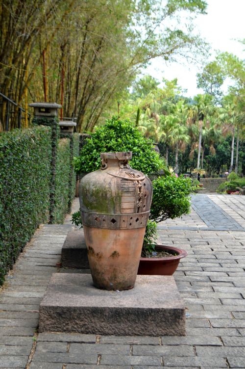 Free A peaceful garden scene featuring a large ceramic pot on a stone slab, surrounded by lush greenery. Stock Photo