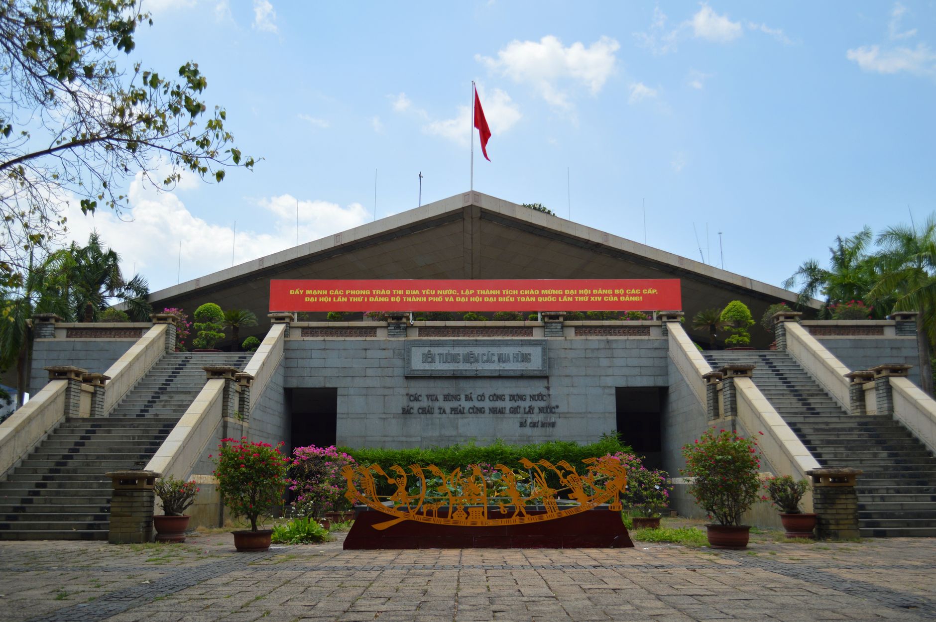 Front view of the Vietnam War Memorial in Hue, featuring a prominent red flag and commemorative sculptures.