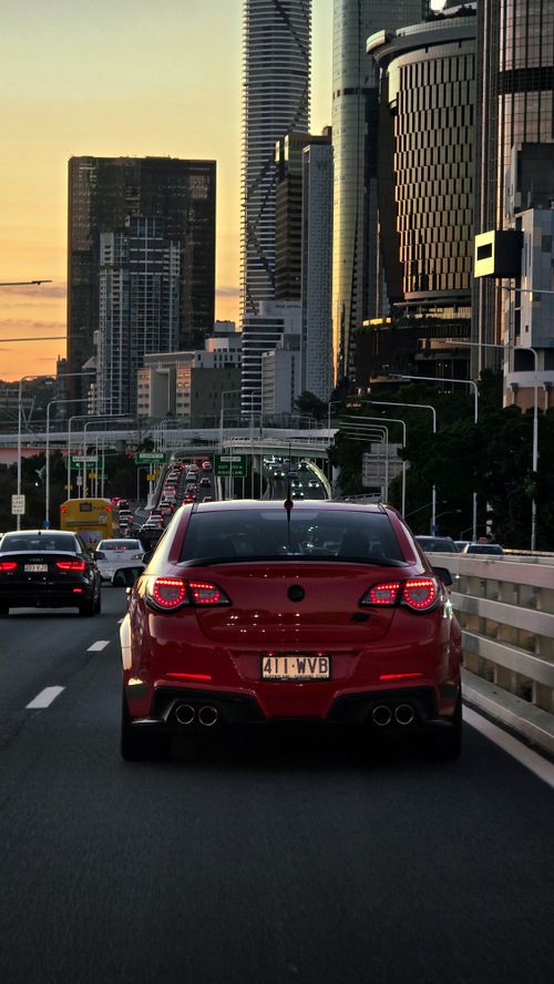 Free Red car driving through city at sunset with skyscrapers in the background, capturing urban life. Stock Photo