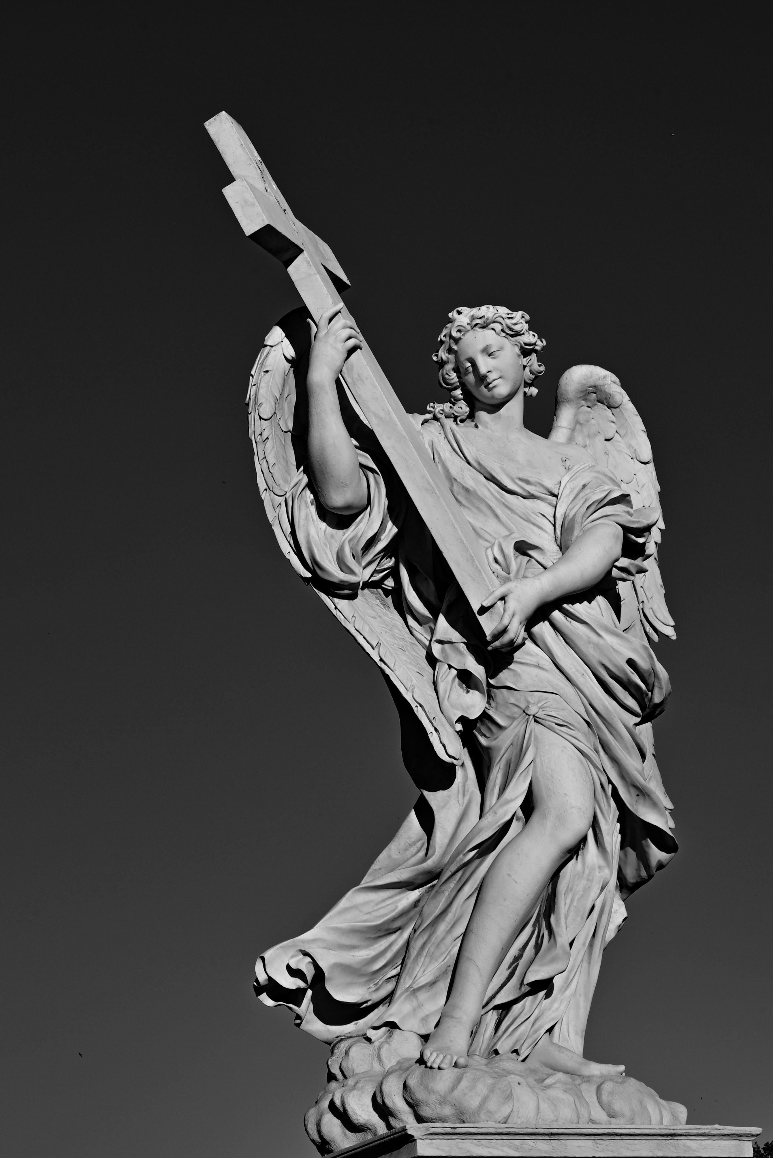 Dramatic black and white photo of angel statue holding a cross on Ponte Sant'Angelo in Rome, Italy.