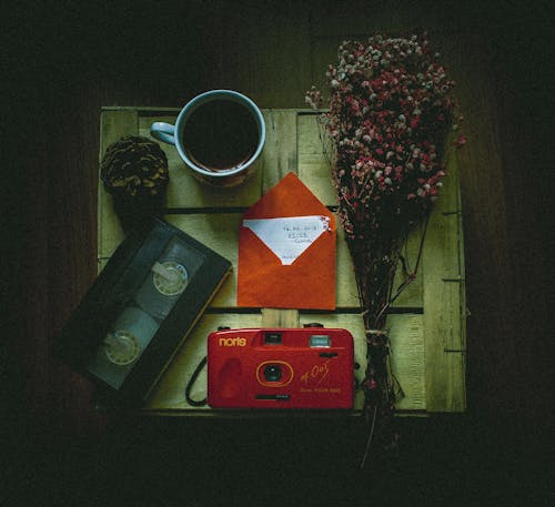 Top view of cup of coffee with bunch of delicate flowers placed near retro photo camera and videotape with envelope