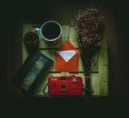 Top view of cup of coffee with bunch of delicate flowers placed near retro photo camera and videotape with envelope