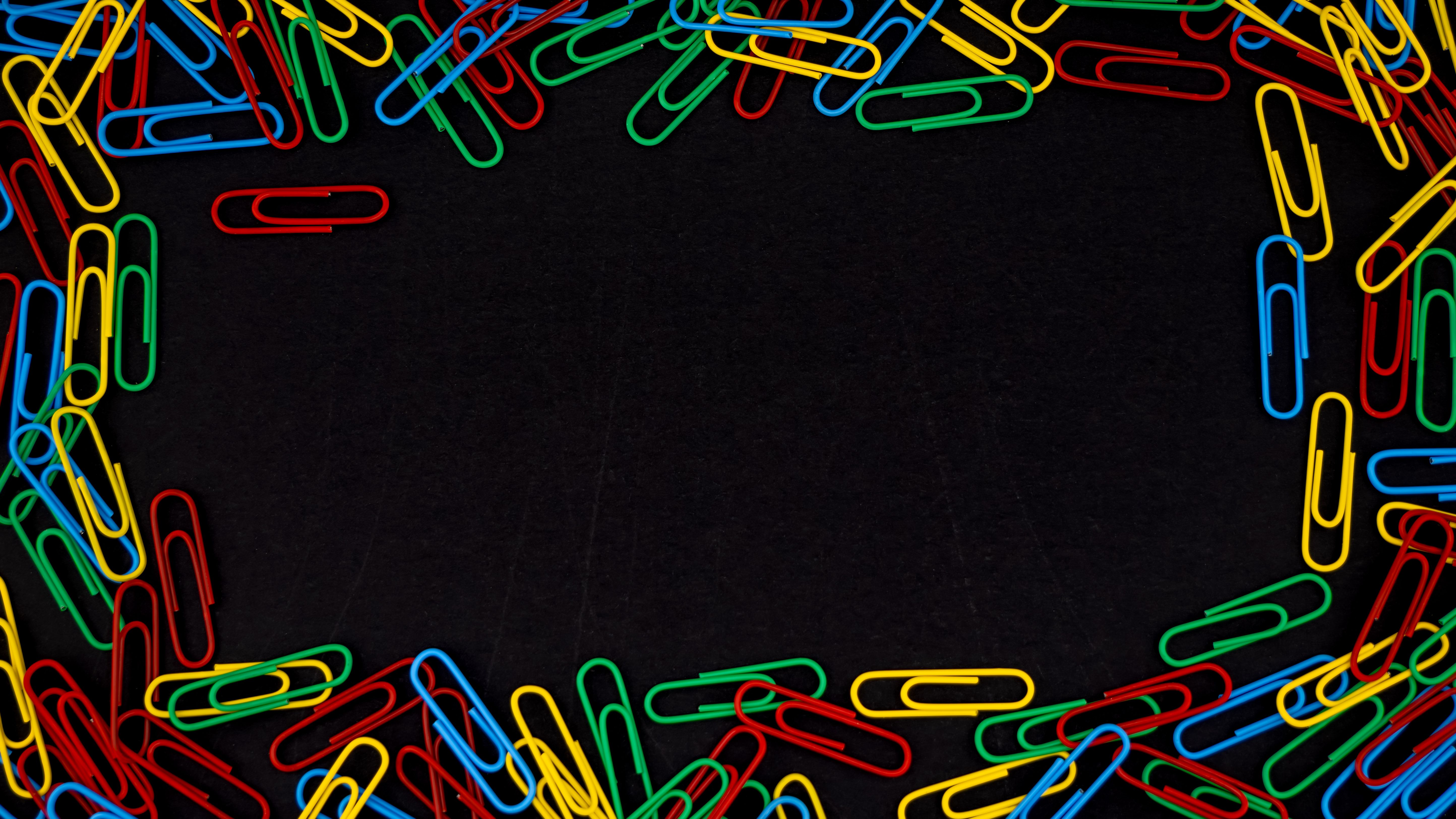 A vibrant assortment of colorful paperclips arranged on a black surface with empty center space.