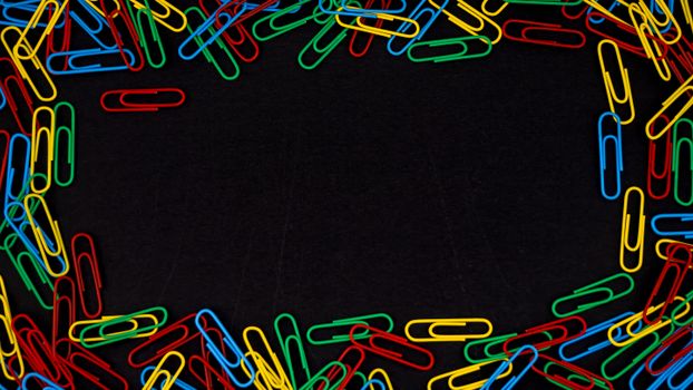 A vibrant assortment of colorful paperclips arranged on a black surface with empty center space.