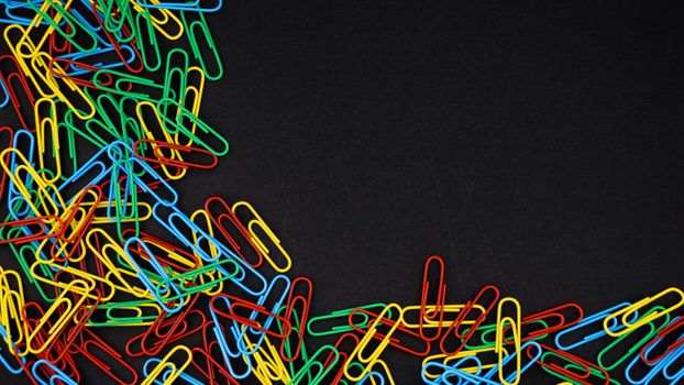 A scattered pile of colorful paperclips on a black background, offering copyspace.