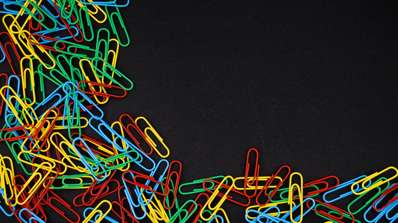a scattered pile of colorful paperclips on a black background offering