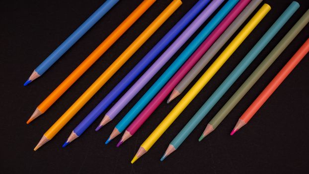 Vibrant colored pencils neatly arranged on a black surface, showcasing artistic flair.