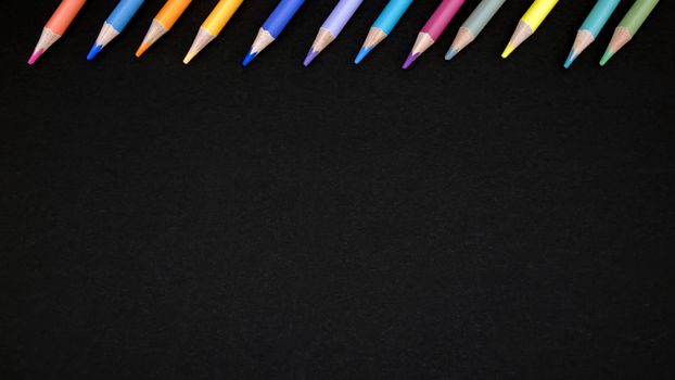 Vibrant colored pencils arranged on a black board, offering ample copy space.