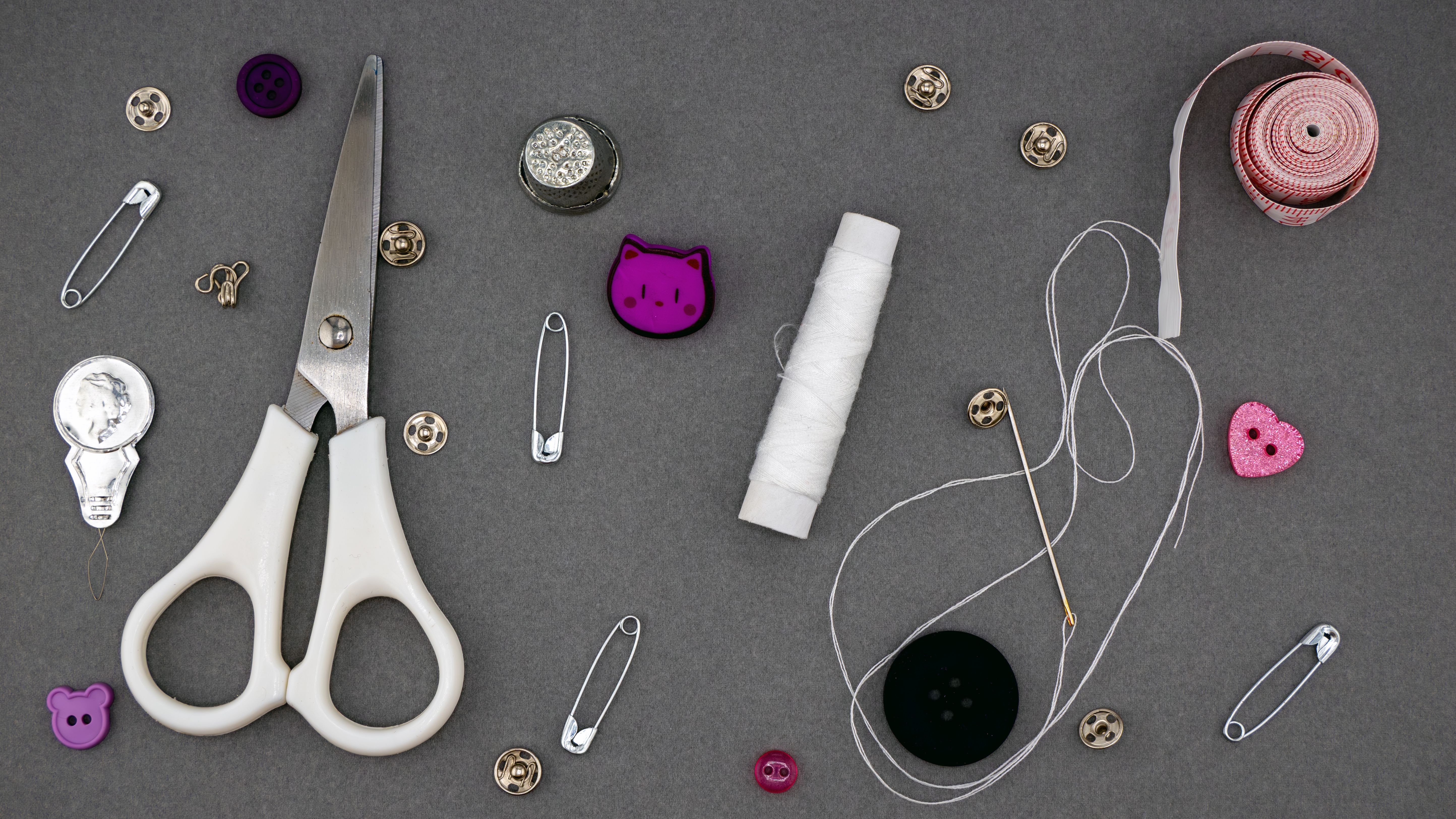 Flat lay of sewing supplies including scissors, thread, and buttons on a gray backdrop.