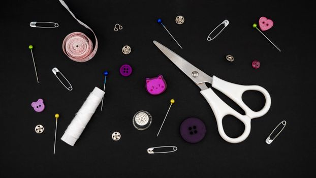 Flat lay of various sewing tools including scissors, pins, and buttons on a black background.