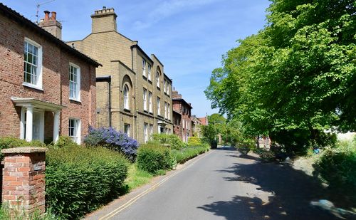 Free Charming suburban street lined with classic brick houses and lush greenery under a clear blue sky. Stock Photo