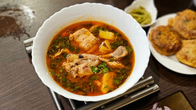 Savory chicken stew in a bowl with herbs and side dishes on a wooden table.
