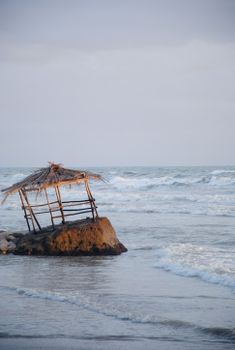 A rustic wooden hut sits on a rock by the sea in Anzio, Lazio, Italy, during a serene dusk.