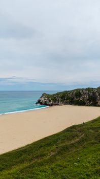 Beautiful Cantabrian beach with cliffs and clear blue sea under a serene sky, perfect travel destination.