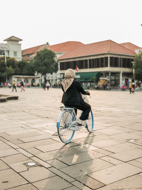 Free A woman in a hijab rides a bicycle in Jakarta's Kota Tua, a historic area known for its Dutch colonial architecture. Stock Photo