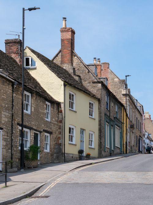 Free Picturesque street lined with classic stone houses in an English village under a clear blue sky. Stock Photo
