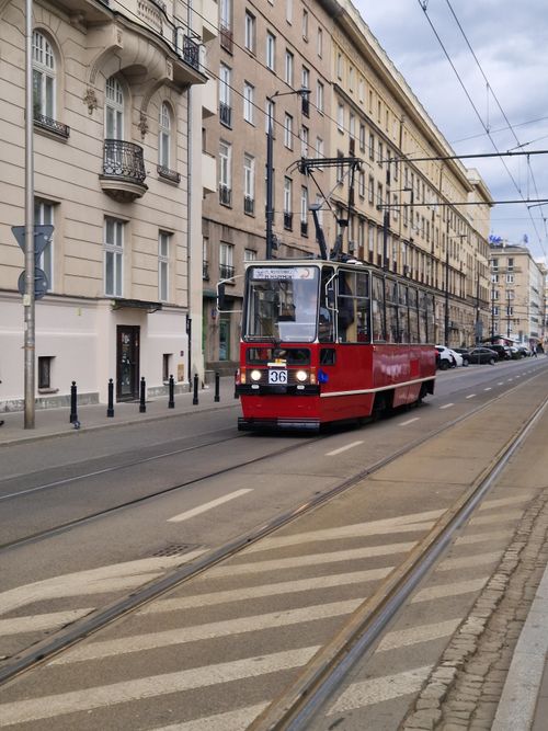 Free A bright red tram travels down a city street in Warsaw, Poland, showcasing urban transportation. Stock Photo