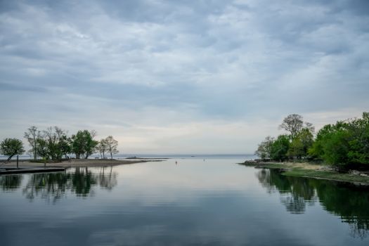 A serene lakeside view with reflections of trees under a cloudy sky.