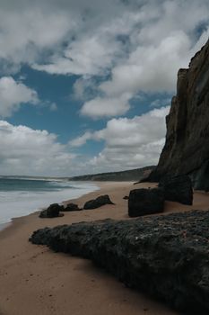 A scenic view of a coastal cliff and sandy beach under a dramatic cloudy sky.
