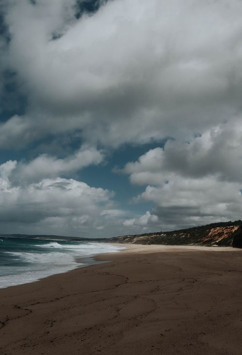 Free Calm beach scene with soft waves and a dramatic cloudy sky, offering tranquility and natural beauty. Stock Photo