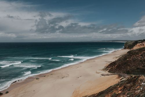 Free Serene view of a deserted beach with waves under a cloudy sky. Stock Photo