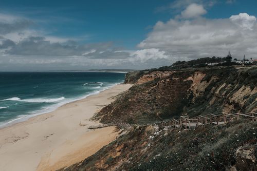 Free A scenic view of a rugged coastline with cliffs and sandy beach under a cloudy sky. Stock Photo