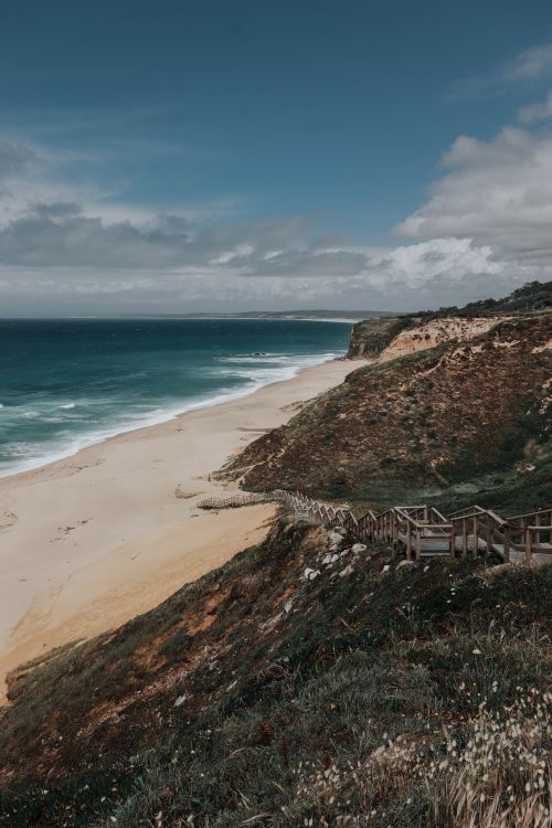 Free A breathtaking coastal landscape featuring a sandy beach and rugged cliffs under a blue sky. Stock Photo