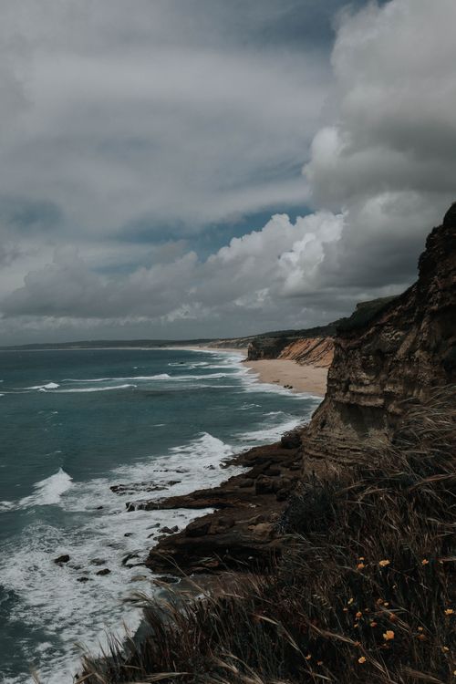 Free A dramatic view of coastal cliffs under a moody sky with waves crashing below, evoking a sense of adventure. Stock Photo