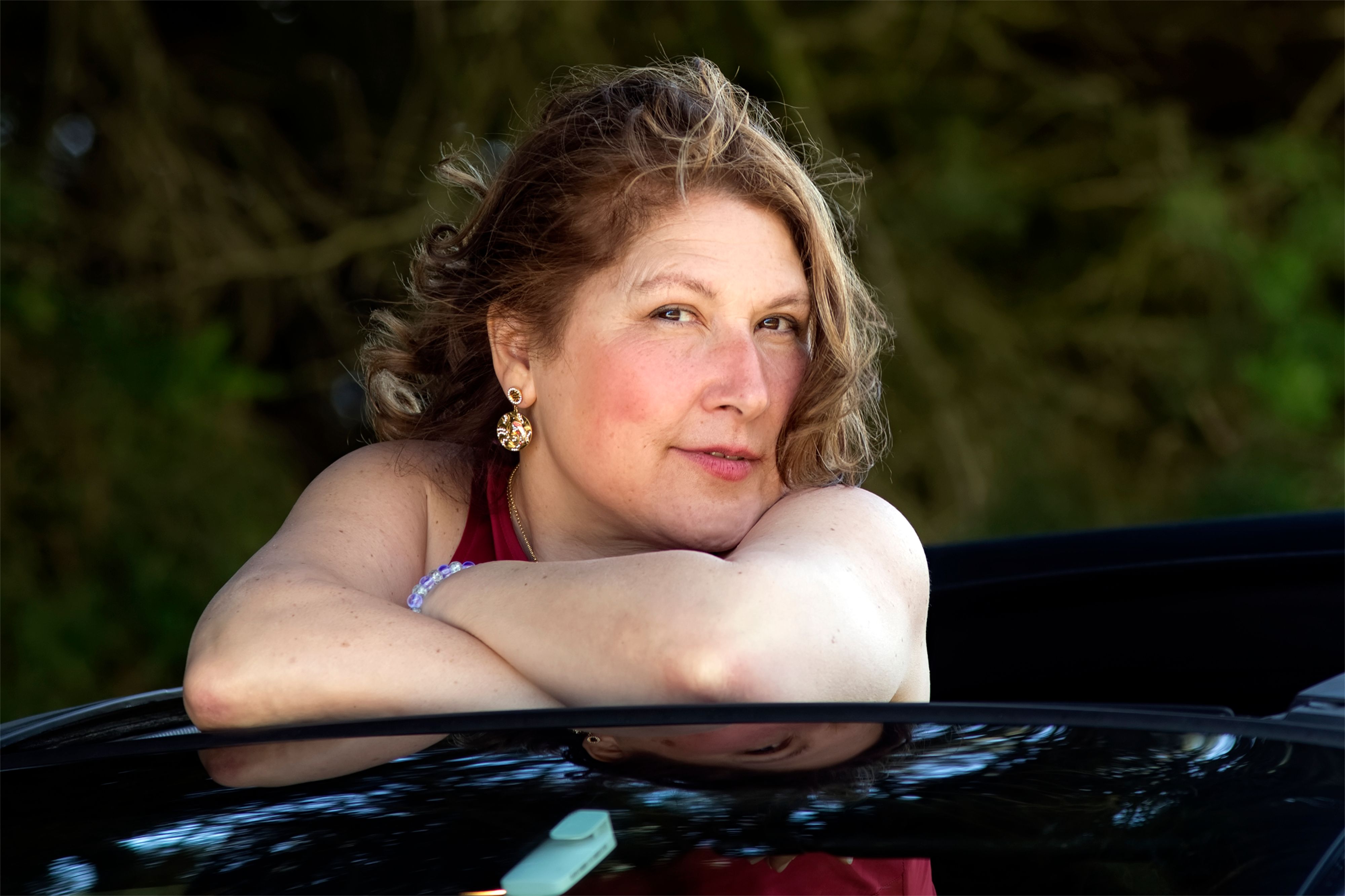 A relaxed woman leans on a car door, embracing the outdoors with a serene expression.