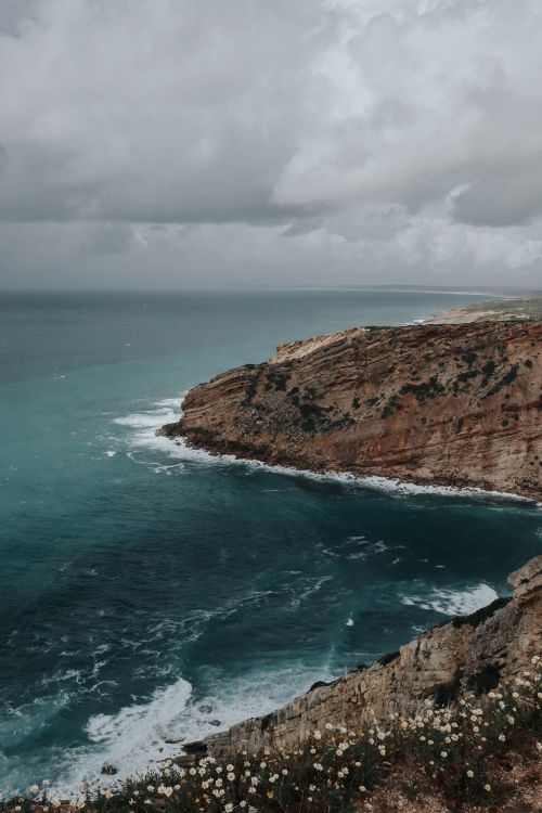 Free Rugged coastal cliffs meet turbulent ocean waves beneath dramatic, overcast skies. Stock Photo