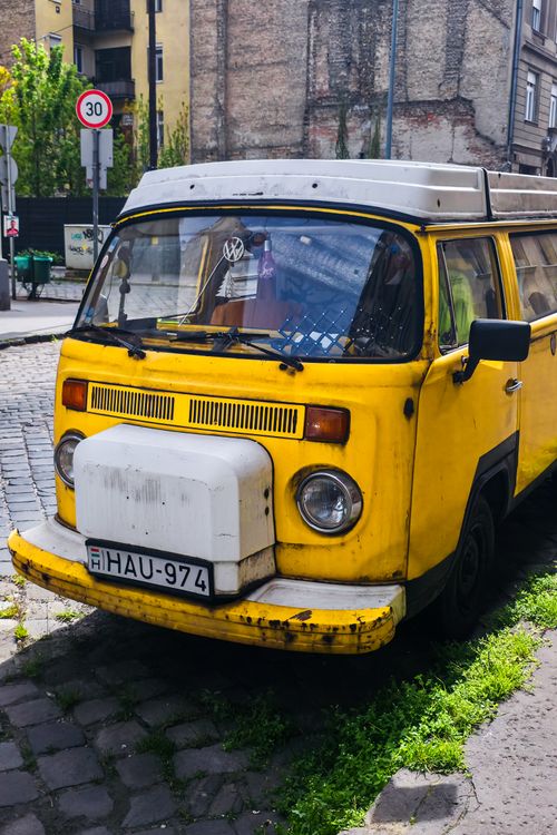 Free Explore the charm of a yellow vintage van parked on a cobbled street in a bustling cityscape. Stock Photo