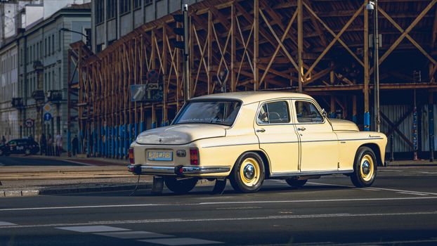 A classic vintage car parked at an urban street corner with wooden scaffolding in the background.