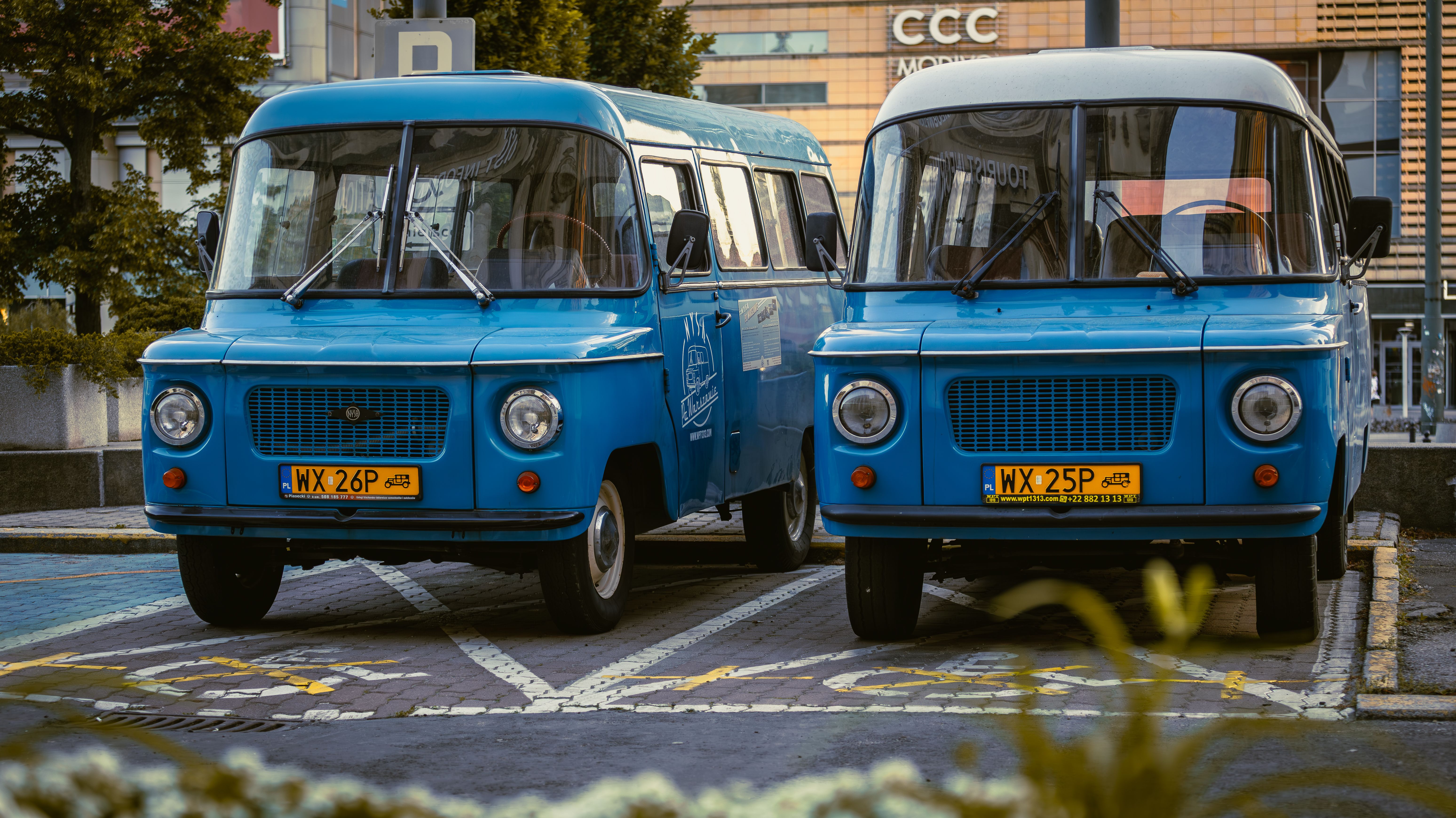 Two retro blue vans parked side by side in a city environment, showcasing classic design.