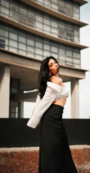 Stylish woman in a white shirt and black skirt posing confidently in front of a modern building exterior.