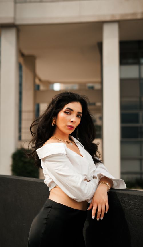 Free Elegant young woman in a white blouse and black pants posing confidently outdoors. Stock Photo