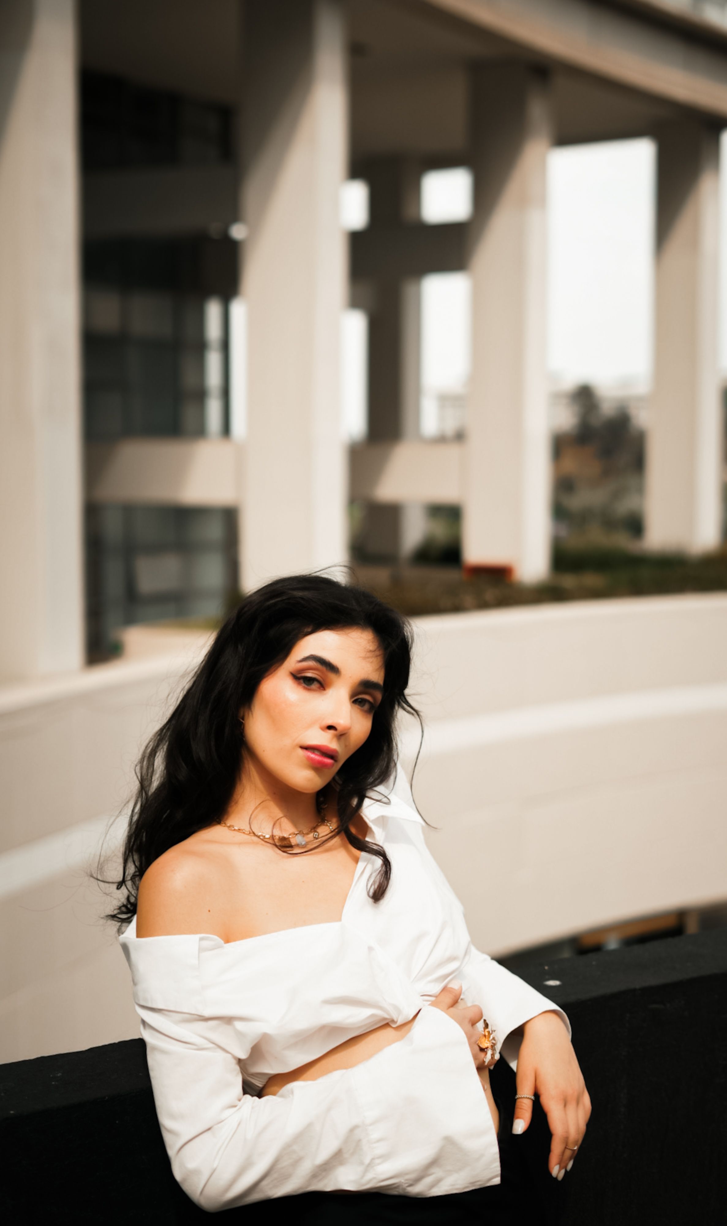 Elegant woman in white blouse poses against modern urban architecture backdrop.