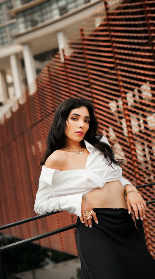 Free Confident young woman in a white shirt and black skirt posing against an urban backdrop. Stock Photo