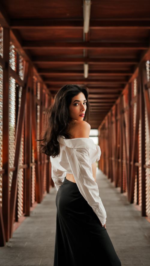 Free Elegant woman in a modern white blouse and black skirt posing in a wooden corridor, exuding confidence. Stock Photo