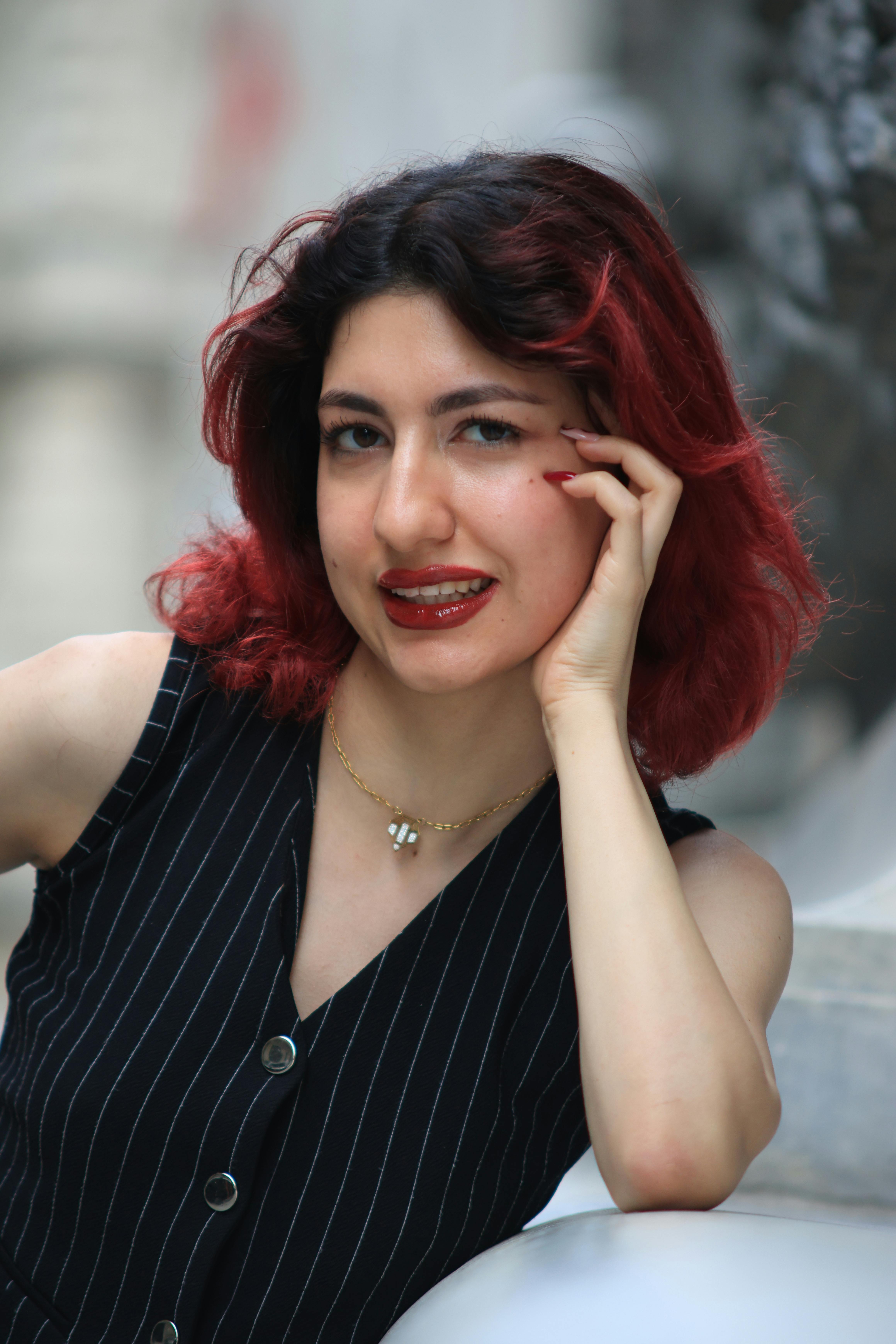 Portrait of a young woman with red hair in a pinstripe outfit, set against a blurred urban background.