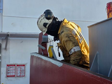 Worker in safety gear painting a red metal structure outdoors, enhancing industrial aesthetics.